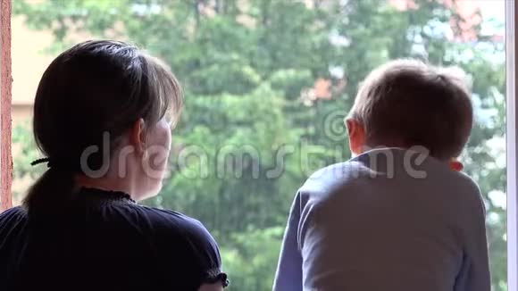 母亲和儿子欣赏窗前的夏雨男孩抚摸着水滴视频的预览图