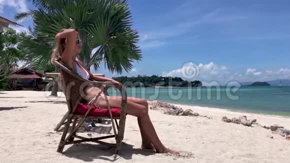 穿比基尼的女人坐在热带海滩的椅子上视频的预览图