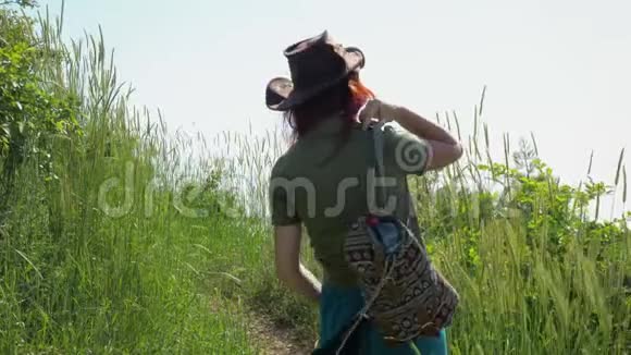 戴着牛仔帽背着背包的红发女孩走在山路上视频的预览图