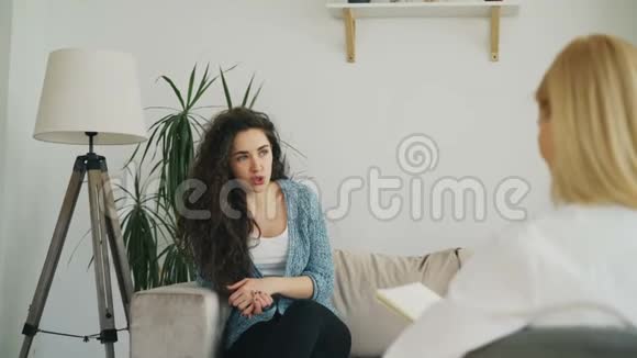 微笑的女人坐在沙发上紧张地与女性精神分析师交谈并在心理治疗师中做手势视频的预览图