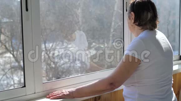 一位老年妇女站在窗口望着街道视频的预览图