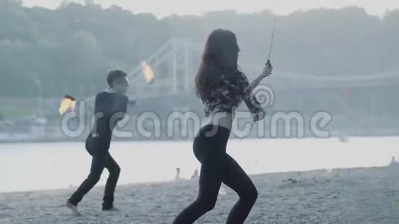 年轻漂亮的女孩和英俊的男人穿着黑色的衣服表演节目火焰站在河岸上那个女人视频的预览图