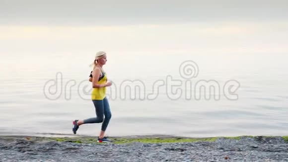 一个穿黄色T恤的女人沿着湖岸或大海奔跑视频的预览图