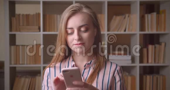 高校图书馆年轻漂亮的高加索女学生用手机特写照片视频的预览图