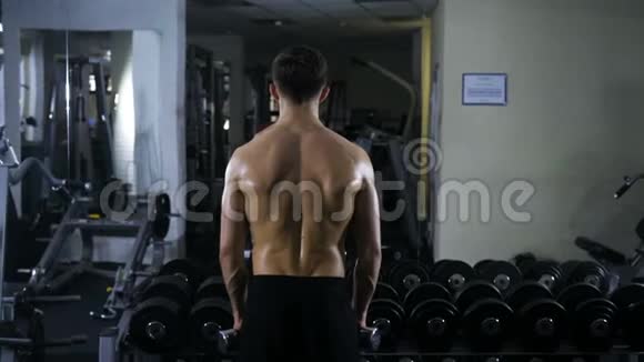 一个运动健将在镜子旁边的健身房用哑铃锻炼手臂肌肉视频的预览图