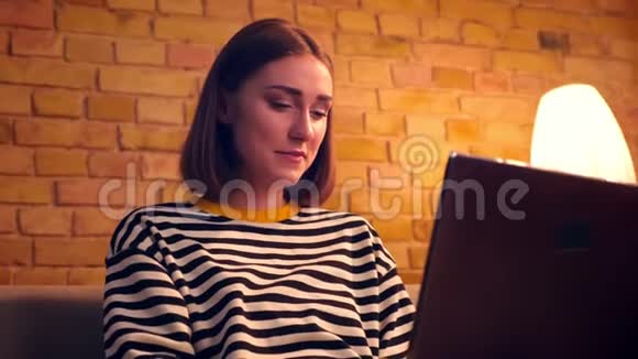 年轻漂亮的女性在网上学习的特写照片笔记本电脑坐在室内舒适的公寓里的沙发上视频的预览图