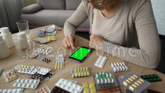 老年妇女滚动智能手机在线医学咨询绿色屏幕视频的预览图