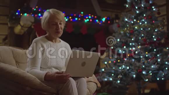 老太太在圣诞树旁用笔记本电脑做视频翻译视频的预览图