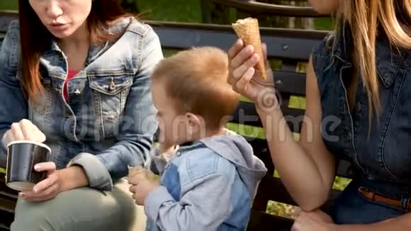 孩子坐在长凳上吃冰淇淋年轻的女人和孩子正在长凳上的公园里吃冰淇淋青年视频的预览图