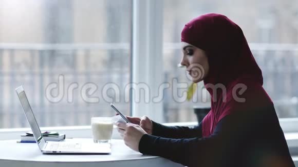 一个迷人的穆斯林女孩使用智能手机和笔记本电脑等不同设备的室内镜头视频的预览图
