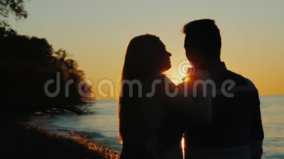日落时分的男人和女人靠近大海太阳光线从后面照得很好视频的预览图