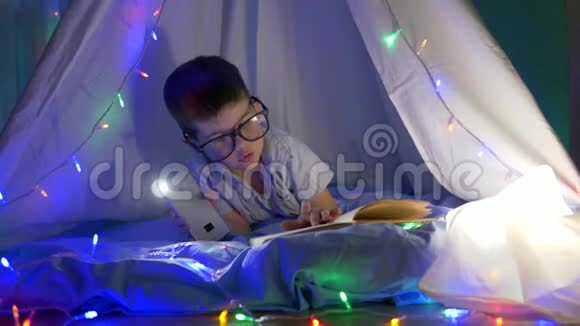 智能幼儿在室内灯光明亮的帐篷里在手电筒照明下阅读眼镜书视频的预览图