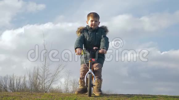 快乐的童年小男孩骑着自行车在大自然的绿草上骑着脚踏车视频的预览图