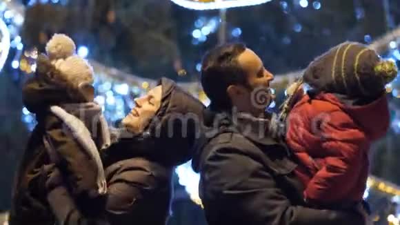 年轻的父母带着孩子跳舞像幸福的家庭一样靠近圣诞树户外视频的预览图