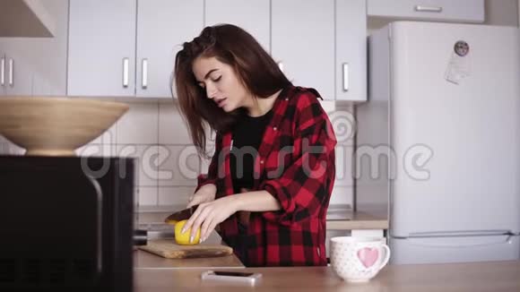 年轻漂亮的女孩穿着红法兰绒衬衫切柠檬然后在厨房里给自己泡了一杯茶视频的预览图
