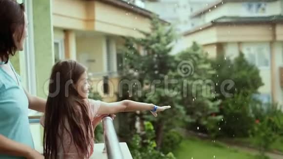 一个女人带着一个10岁的女儿去阳台欣赏夏天的雨视频的预览图