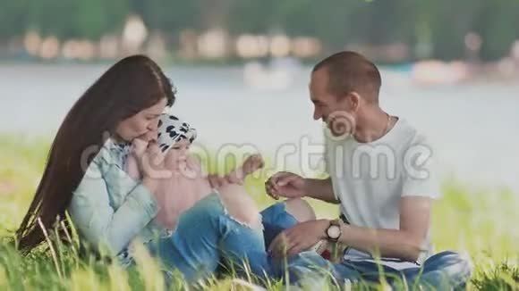 一家三口人坐在河边的草地上的草地上年轻的父母和她女儿一起玩带她去视频的预览图