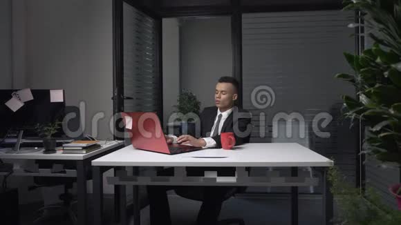 一位年轻成功的非洲商人坐在办公室里用笔记本电脑工作喝着杯子里的咖啡60英尺视频的预览图