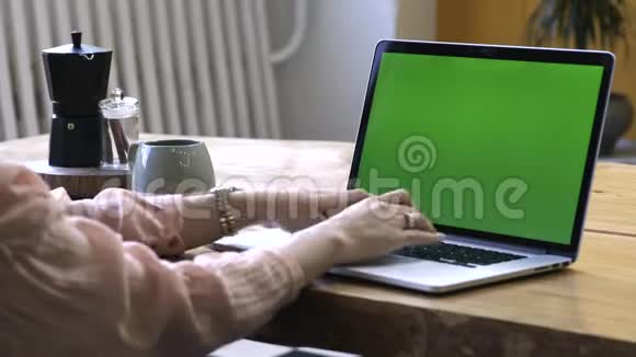 穿着粉红色衬衫的年轻女子坐在大木桌旁用彩色钥匙绿色屏幕在笔记本电脑上打字股票视频的预览图