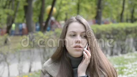 年轻女子微笑着在公园里用手机说话视频的预览图