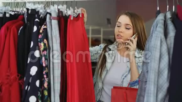 漂亮的女孩在现代商店里选择衣服在手机上聊天彩色裙子和彩色裙子的特写镜头视频的预览图