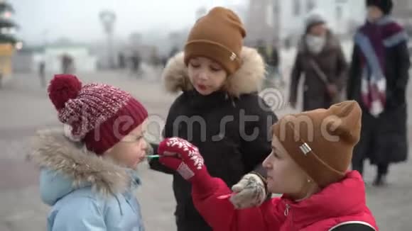 在圣诞树附近的广场上年轻的女人和两个男孩在吃气泡饼视频的预览图