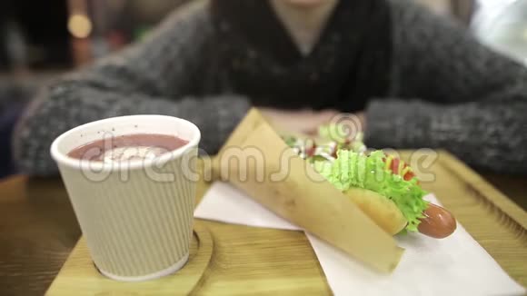 一个漂亮的女孩喝着覆盆子的热饮一条多汁的开胃热狗就在前景中视频的预览图