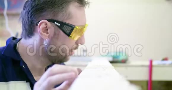 木工车间一人戴防护眼镜清理木板从木板上吹锯屑视频的预览图