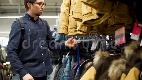 成年男子在一家有衣服的运动商店里寻找和触摸冬季夹克视频的预览图