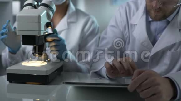 科学家在同事显微镜下观察样品的平板电脑上打字视频的预览图