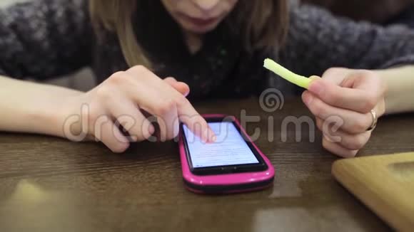 一个漂亮的女人坐在咖啡馆里看着智能手机上的一个网站吃着炸薯条一个年轻女孩视频的预览图
