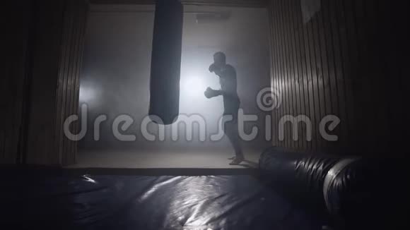 拳击手击打袋在黑暗的健身房慢动作在室内训练的年轻人视频的预览图