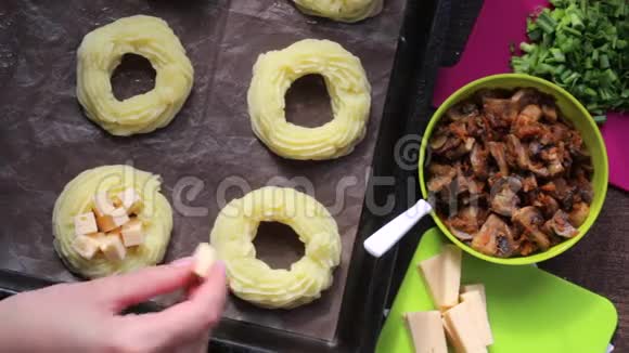 一个女人在烤盘上装满奶酪戒指土豆泥旁边的其他食材做菜饭视频的预览图