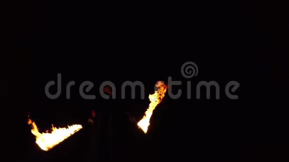穿着黑色西装的劫匪在两个燃烧的火炬上吹气并引发火焰慢速运动视频的预览图