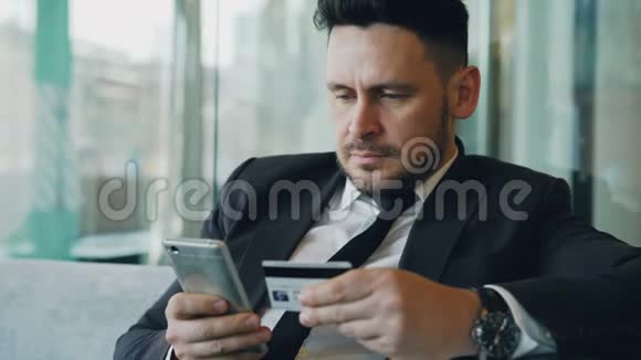 快乐的白人商人穿着正式服装在网上付账手里拿着信用卡和智能手机视频的预览图