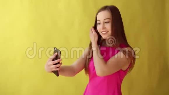 年轻美丽的女士站在黄色背景上被隔离同时通过电话自拍视频的预览图