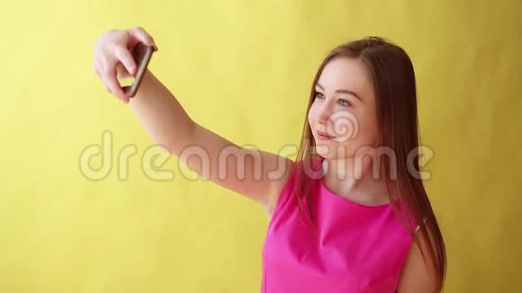年轻美丽的女士站在黄色背景上被隔离同时通过电话自拍视频的预览图