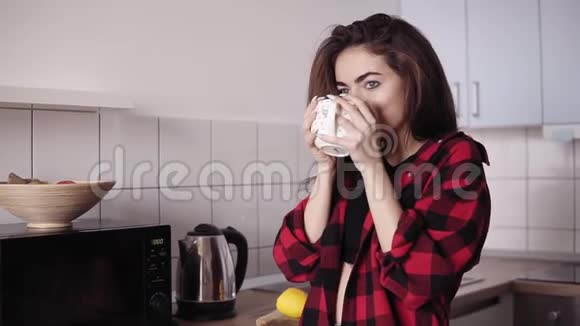 年轻漂亮的女孩穿着法兰绒衬衫一边喝茶一边在舒适的阁楼里做梦视频的预览图
