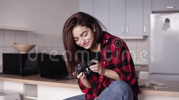 迷人的黑发女孩正试图改变相机设置而坐在她的厨房里穿着法兰绒衬衫和视频的预览图
