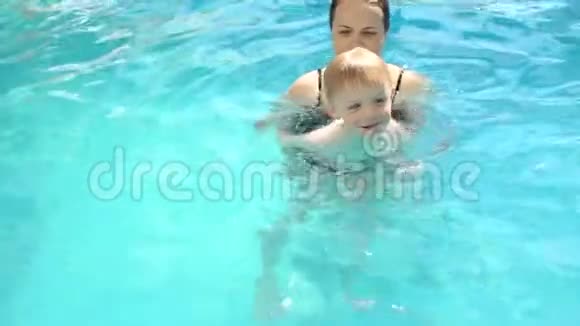 一个年轻的女人教一个孩子在游泳池里的水里游泳视频的预览图