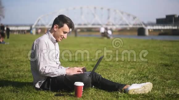 一个人坐在草地上的公园里一个自由职业者做得很好休息微笑夏天有笔记本电脑的人视频的预览图