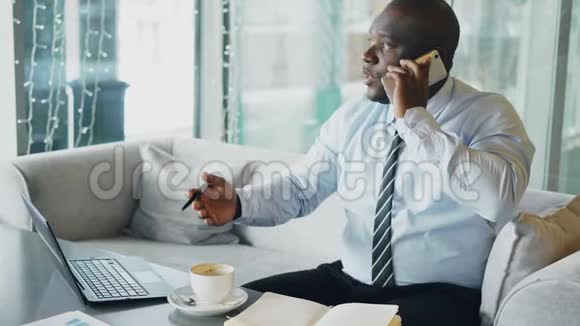 非裔美国商人在智能手机上聊天并把商业信息放在笔记本上视频的预览图