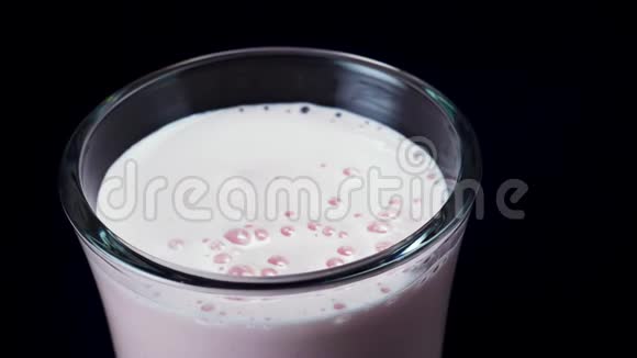 关闭一个装满草莓奶昔的玻璃在黑色背景上隔离框架一瓶粉色冰沙健康视频的预览图