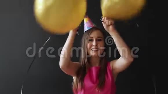 可爱的黑发女人拿着黑色背景上的金色气球视频的预览图