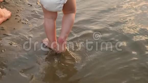 妈妈在海滩上用手牵着尿布的小孩婴儿的脚沿着海滩上清澈的水走慢动作视频的预览图