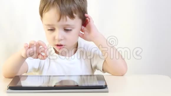 小男孩坐在桌子旁玩平板电脑特写孩子在玩电子游戏运动相机滑块视频的预览图
