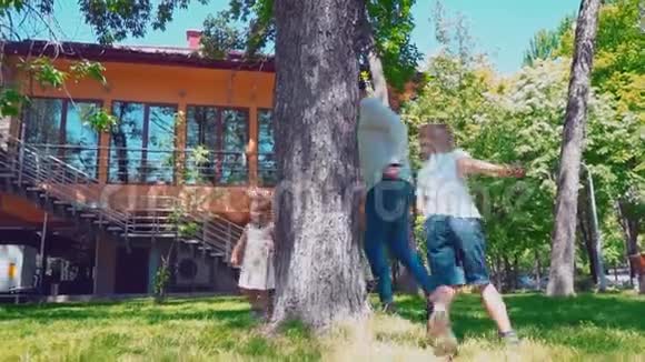 年轻的父亲带着孩子在房子附近的一棵树上跑来跑去爸爸儿子和小女儿在后院玩得很开心视频的预览图