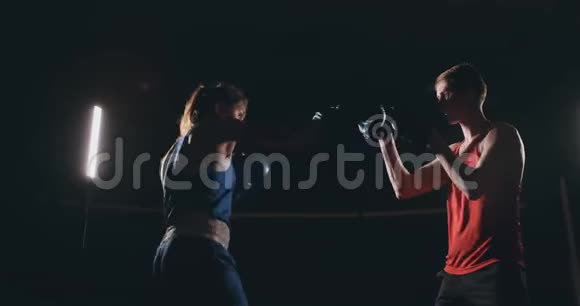 一个漂亮的黑发拳击手在黑暗的房间里和一个教练一起打爪子视频的预览图