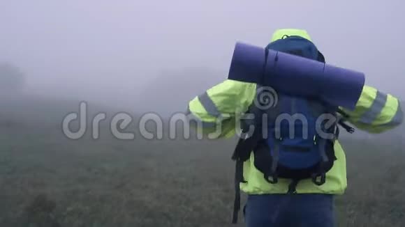 一位身穿信号背心头罩背包在雾中漫步的男子游客的肖像视频的预览图