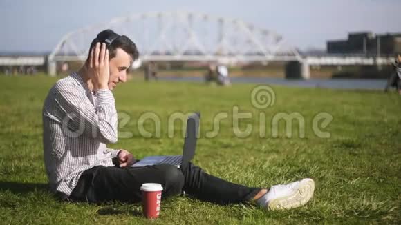 一个男孩坐在公园的草地上在视频交流中交谈一个学生一个自由职业者微笑和微笑每杯咖啡视频的预览图